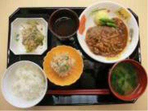 手前左に米飯、右に汁物、それ以外に４つのおかずを載せた黒いトレー