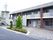 2階建てのタイル張りの建物。2階にはベランダがある。2階から使用できる階段がある。ロータリーがあり、木が植えてある。