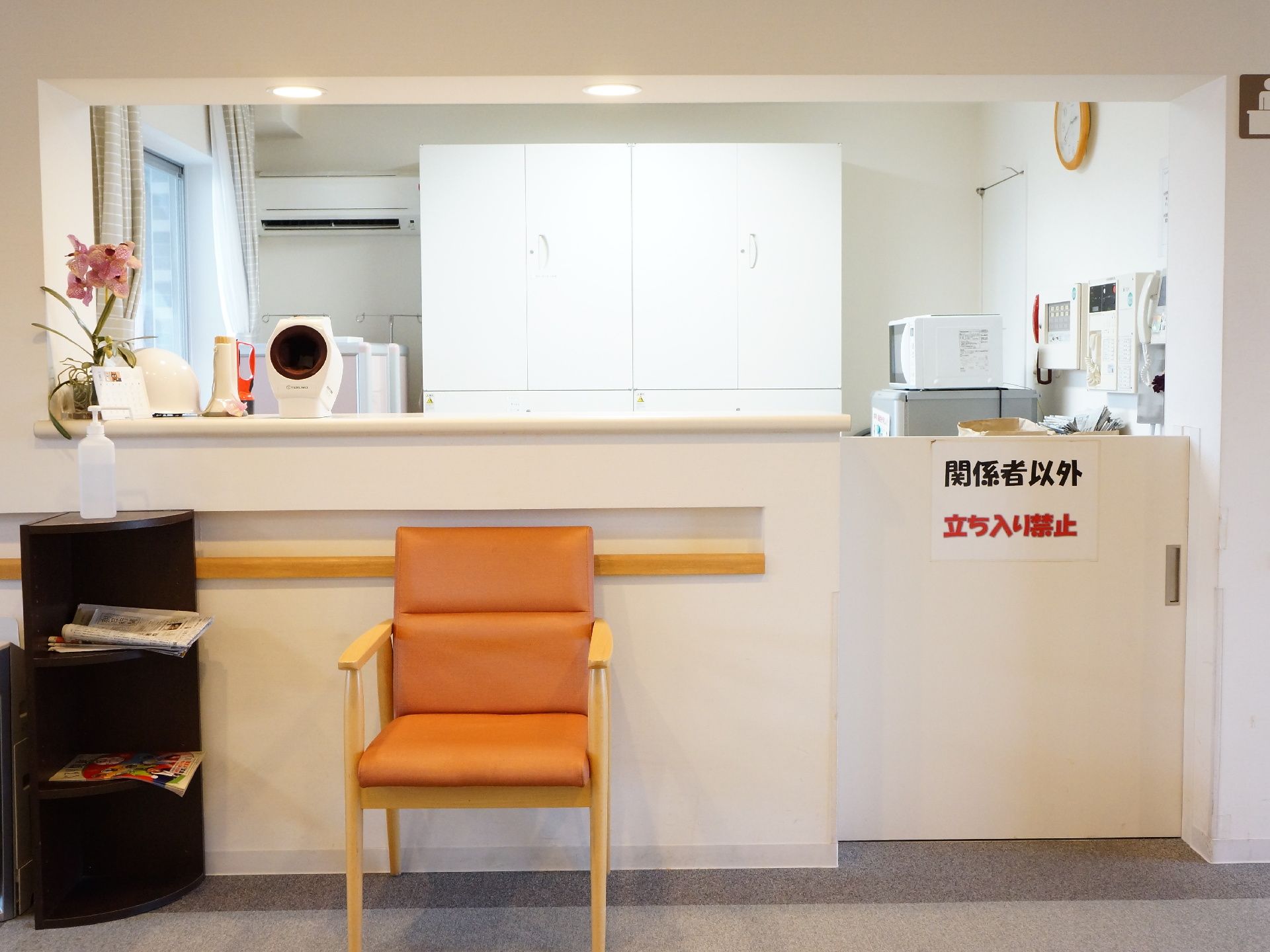 左側に黒いカラーボックスがあり上に消毒スプレーが置かれている。手前に椅子があり、内部には電子レンジなどが置かれている。