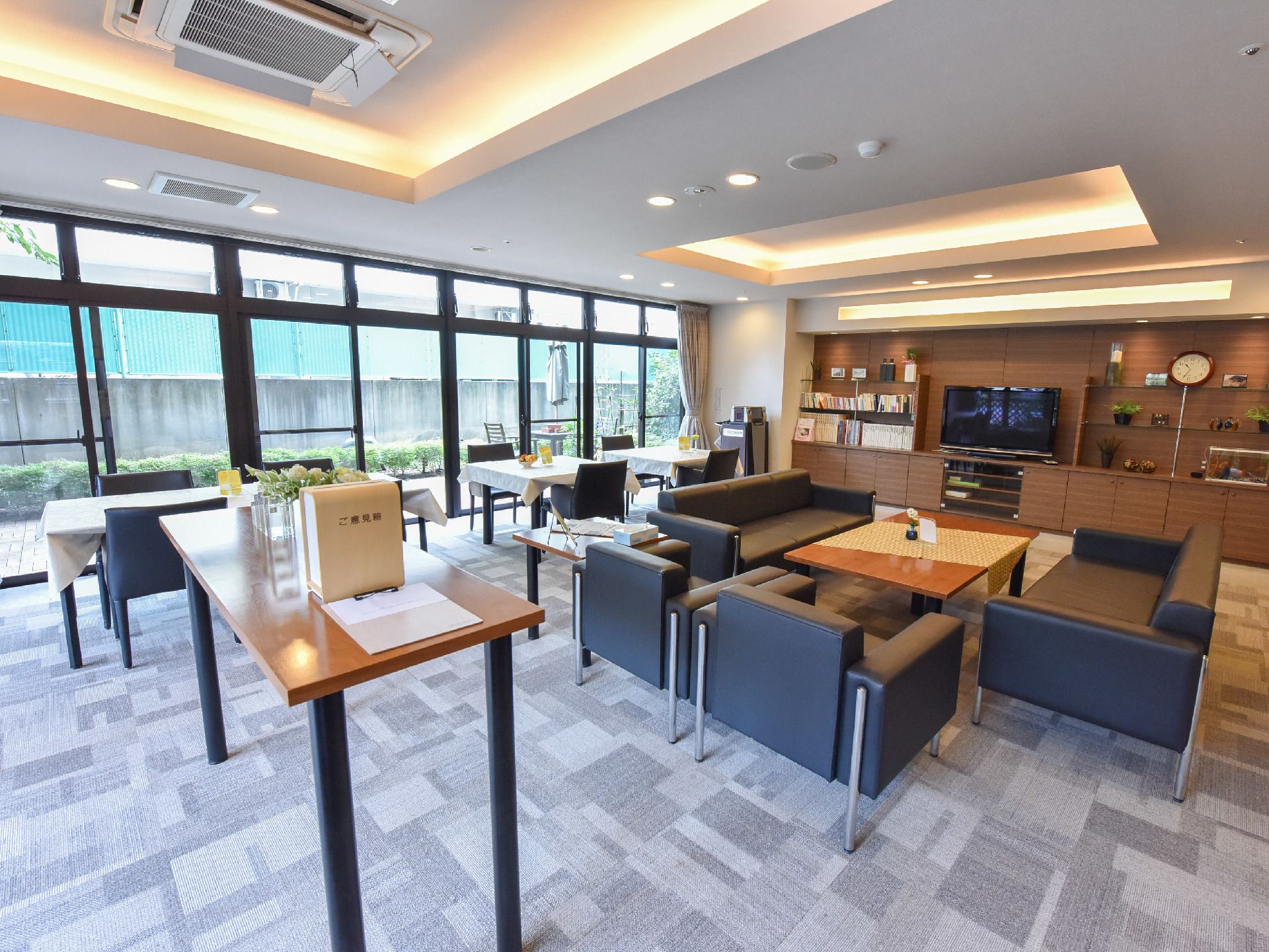 テーブルとソファが並べてあり、正面は、焦げ茶色の収納棚スペース。中央にはテレビが置かれ、両側には本屋や飾り物が置かれている。