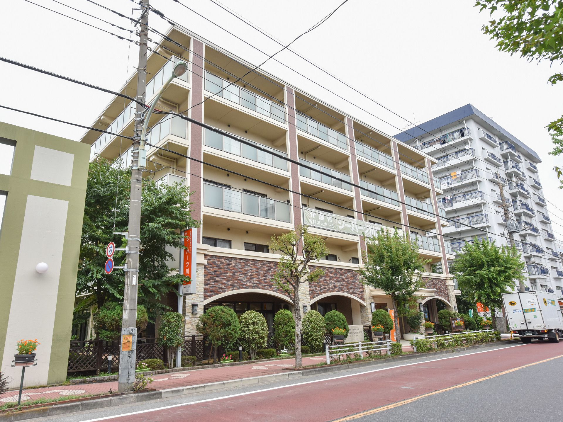 建物前や横には植木が植えられ緑豊かな5階建てのお洒落な建物。街の歩道に位置し、建物の端には施設名の看板が掲げてある。