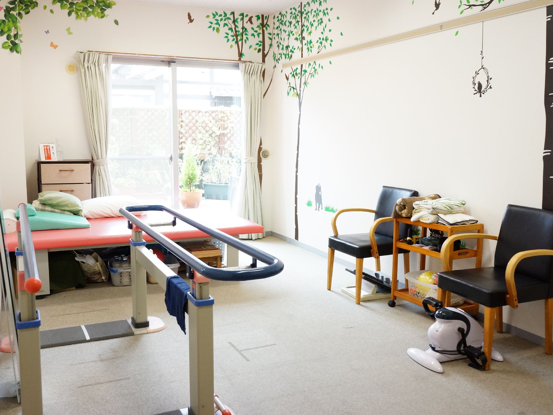 白い壁紙の小部屋には、歩行訓練に使用する手すりや、椅子に座ってペダルをこぐことができる小型のマシンが置かれている。