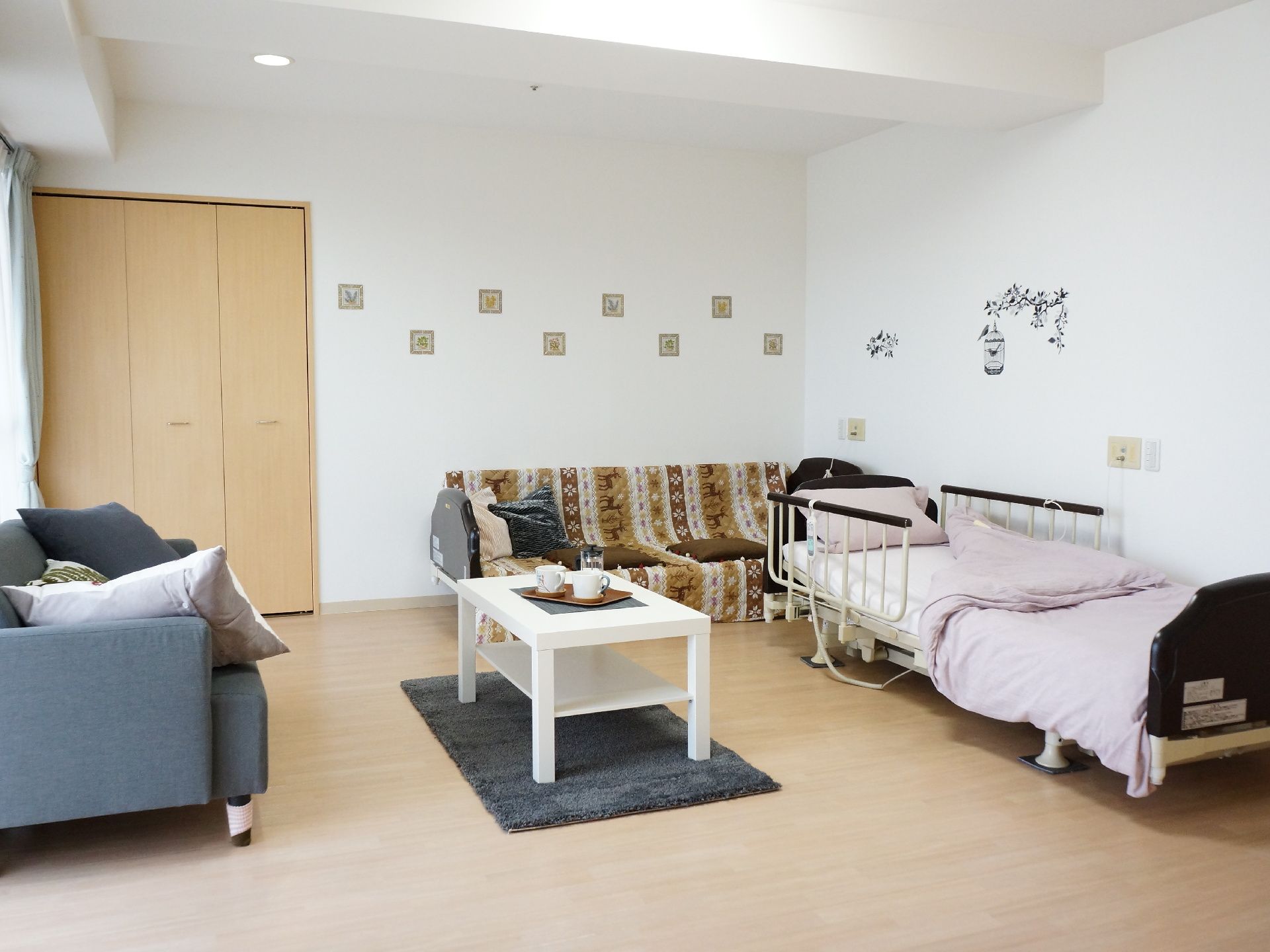 居室はベッドを置いてもゆとりのある広さがある。壁には収納が付いている。窓辺にソファーが置かれている。