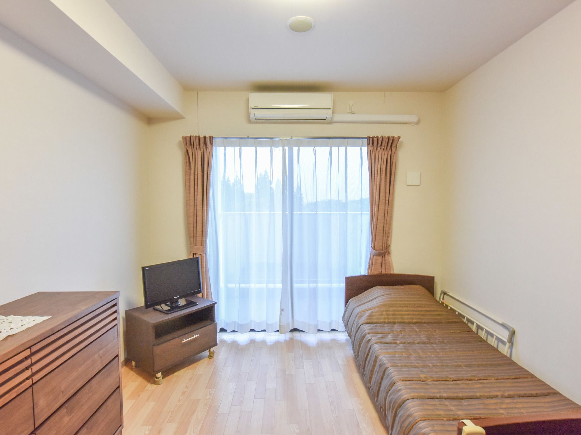 カーテンがかかった窓がある部屋にはベッドが置かれている。タンス、テレビボードに置かれたテレビもある。