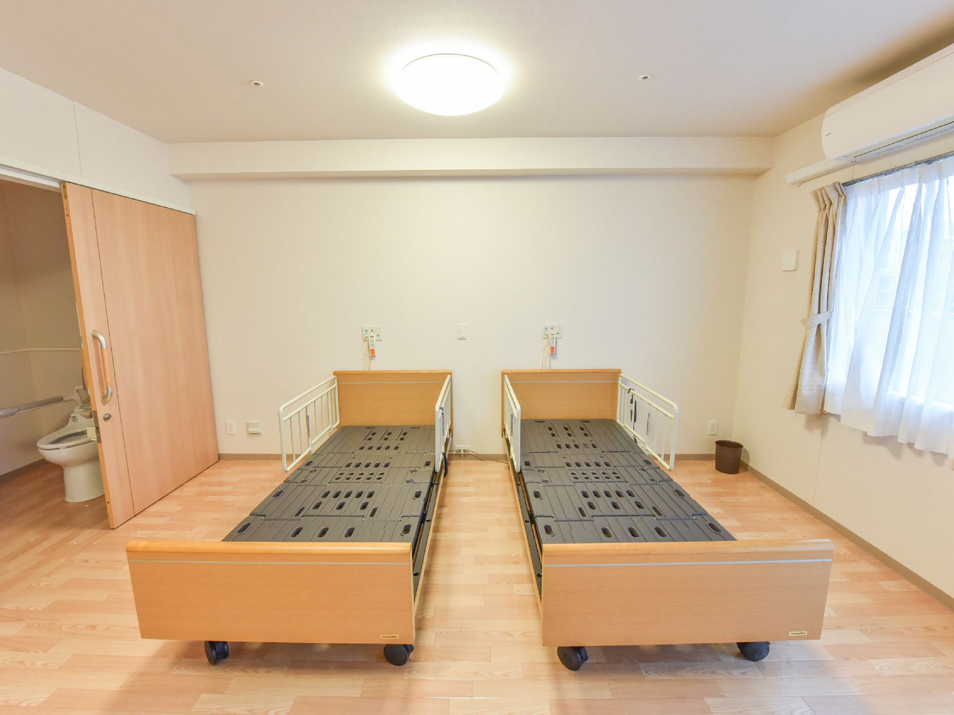 広々とした部屋にはベッドの枠組みが2台置かれている。ベッドの両側半分には柵が付いている。部屋の角にはゴミ箱がある。