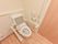 ナチュラル色のフローリングと木目調の扉が取り付けられたトイレの洋式便器の両側には肘置きがついているため、用を足す際に便利である。