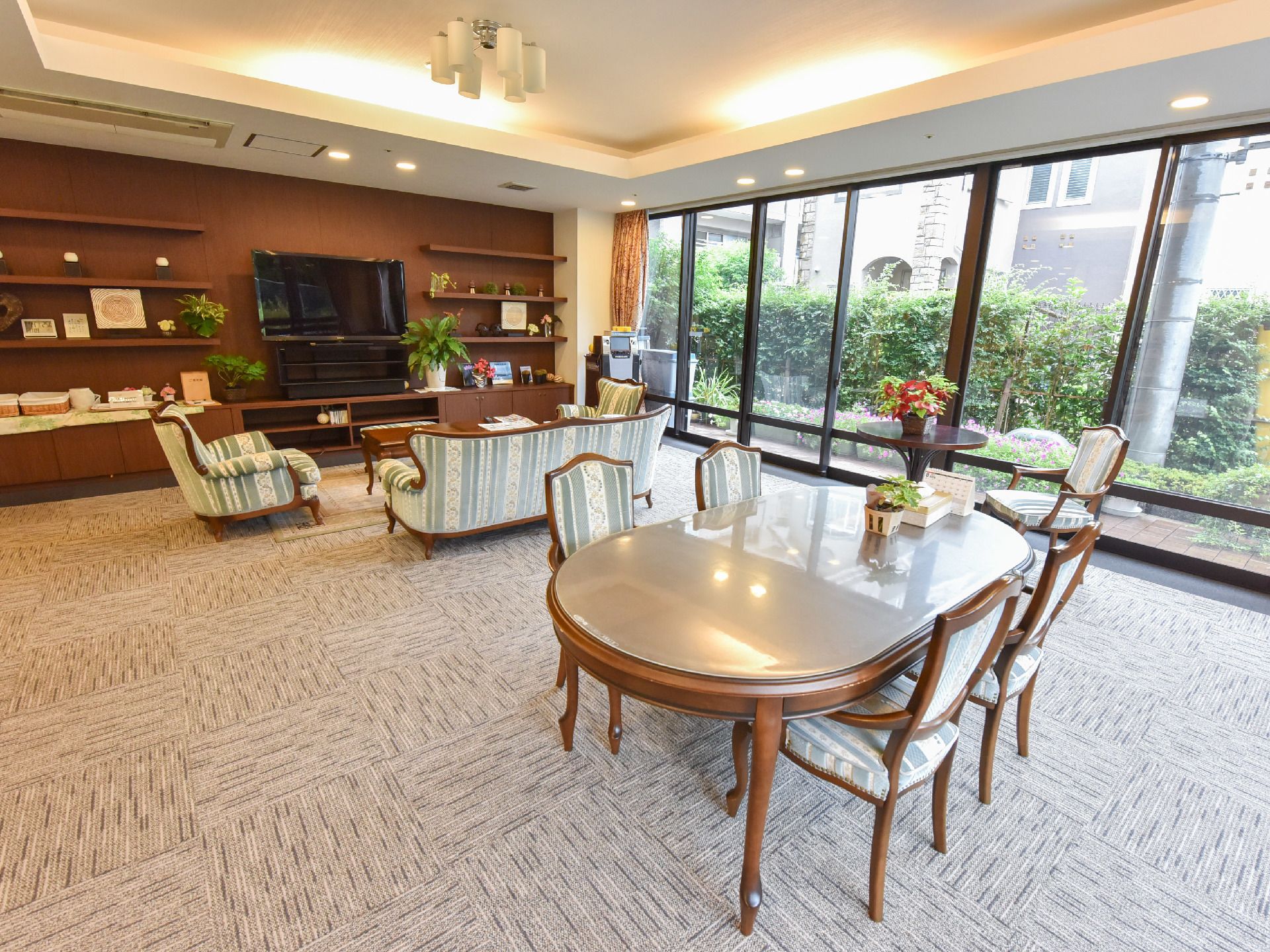 大きな窓がある部屋にはテレビが置かれている。また、3つの大きさや形の異なるテーブルと肘置き付きの椅子、ソファーが置かれている。