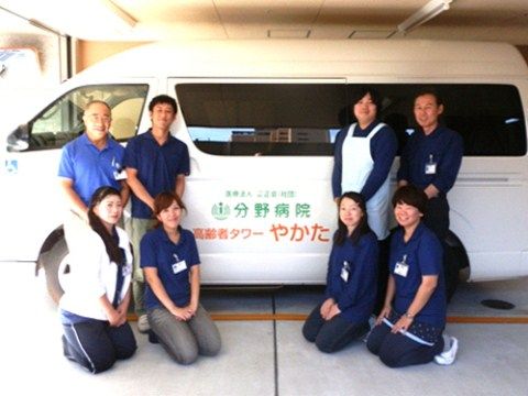 施設の名前の入った白いワゴン車の前にいる8人の男女スタッフ