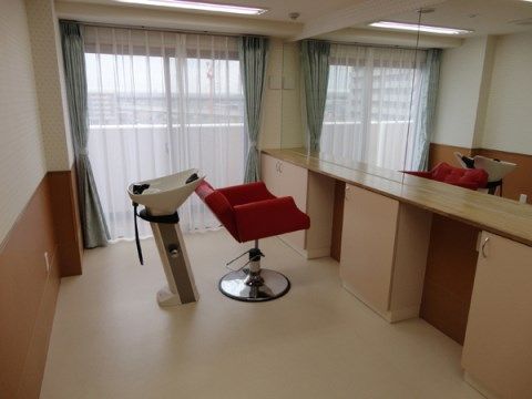 一面の鏡張りの前に、赤い椅子と洗面ボウルがある理美容室