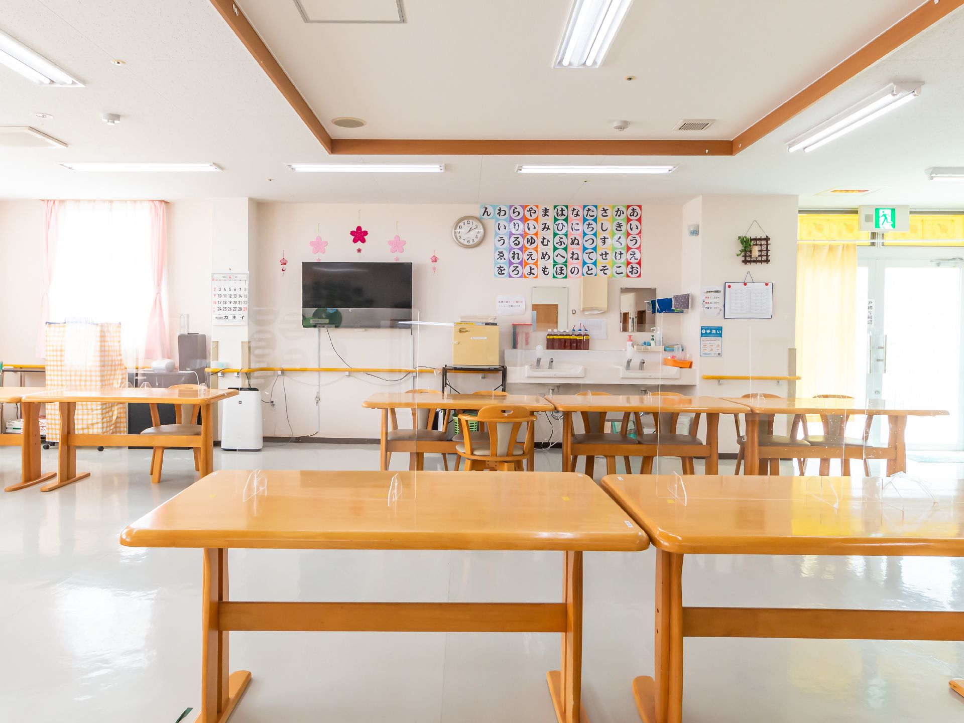 壁も床も白い食堂に並ぶ、明るい茶色の木製テーブルと椅子