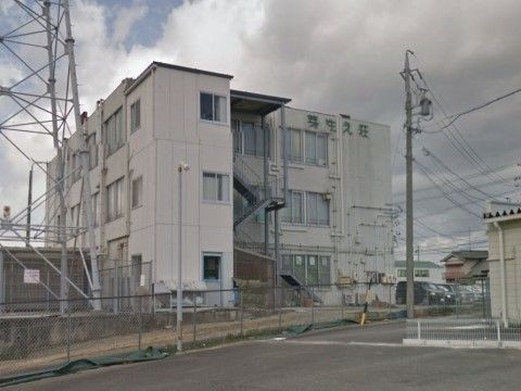 鉄塔のそばに建つ、非常階段のついた３階建ての白っぽい建物