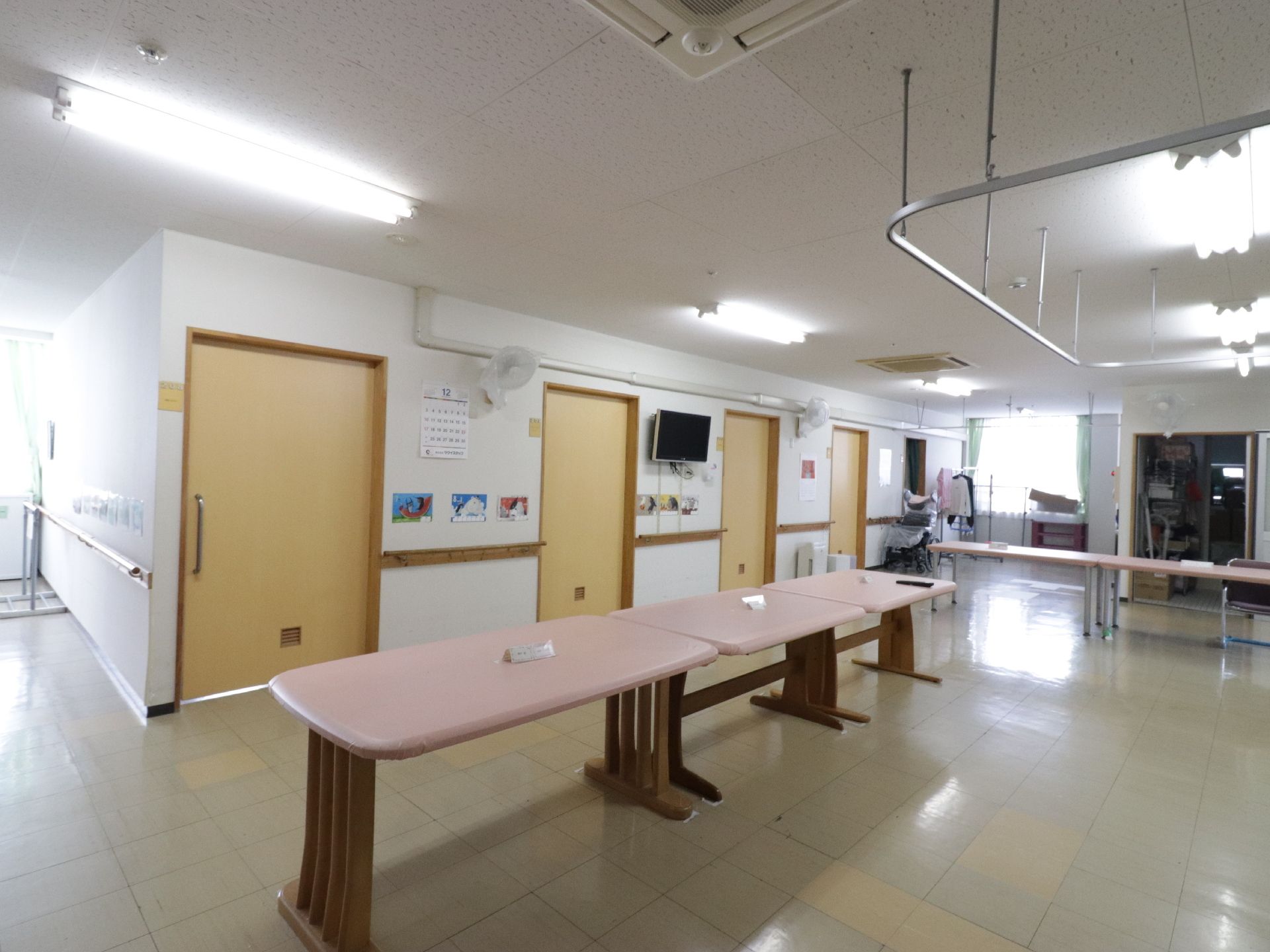 何枚かのスライドドアの前に、いくつかピンク色の机が置かれた共有スペース