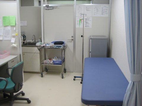 小さなベッドやデスクが置かれ、ワゴンや医療器具がある診察室