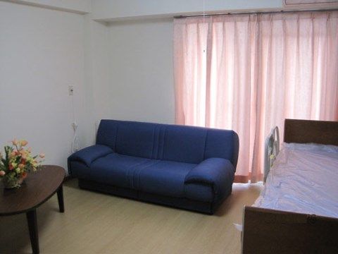 正面に窓があり、上の天井近くにはエアコンが設置してある。窓の前には平行にソファが置かれ、壁際にベッドがある。