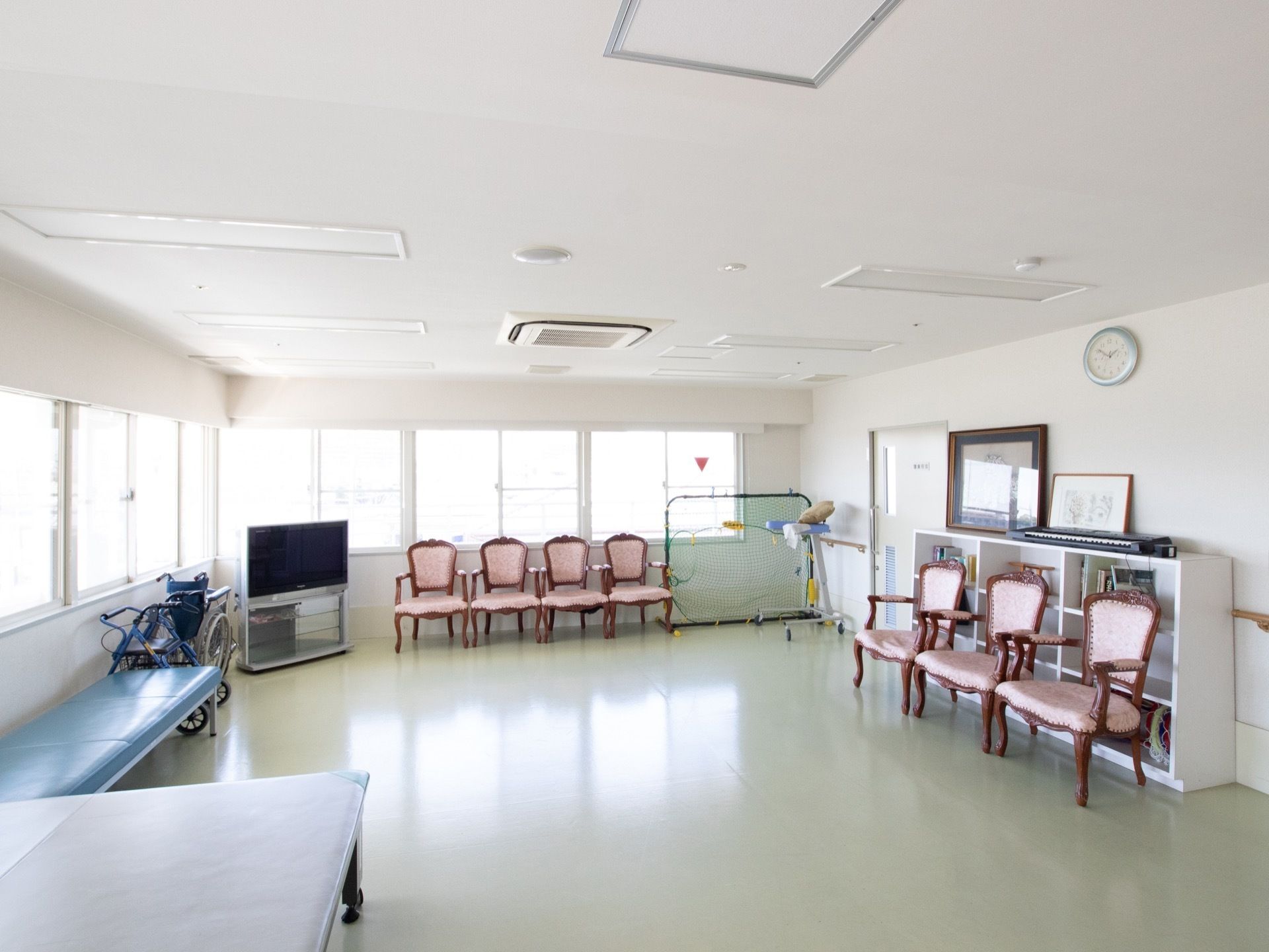 壁際に椅子や台などが寄せられており、車椅子も備えつけられている。また、部屋の隅にはテレビやさまざまな道具が乗った棚が置いてある。