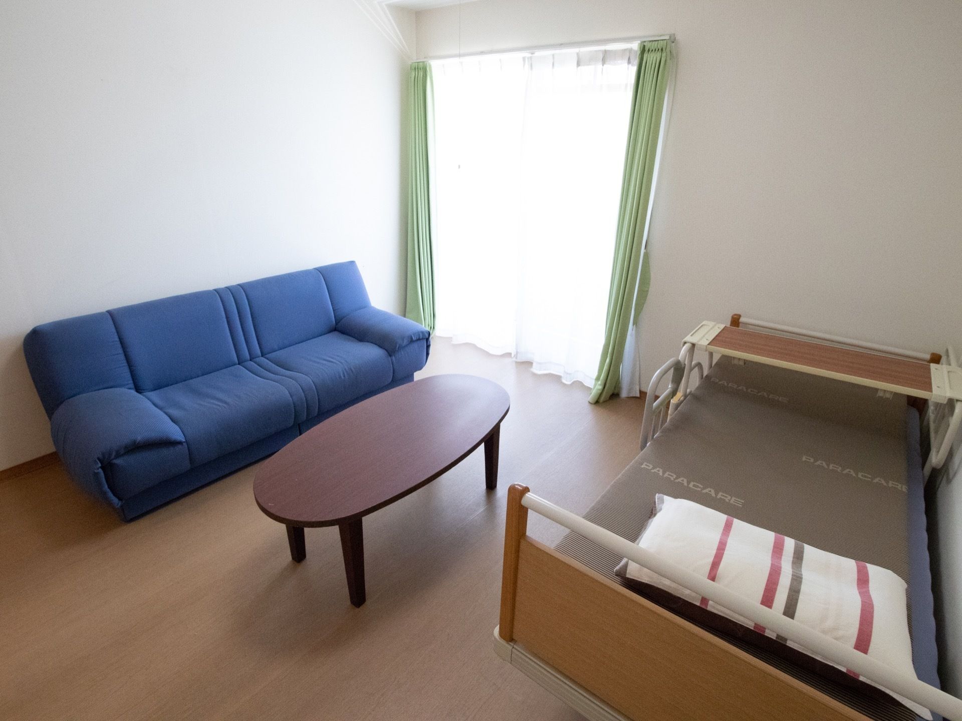 青色のソファと、茶色の低い机と布団などが敷かれていないベッドがおいてある。ベッドの上には枕がおいてあり、足元には専用の机が備えられている。