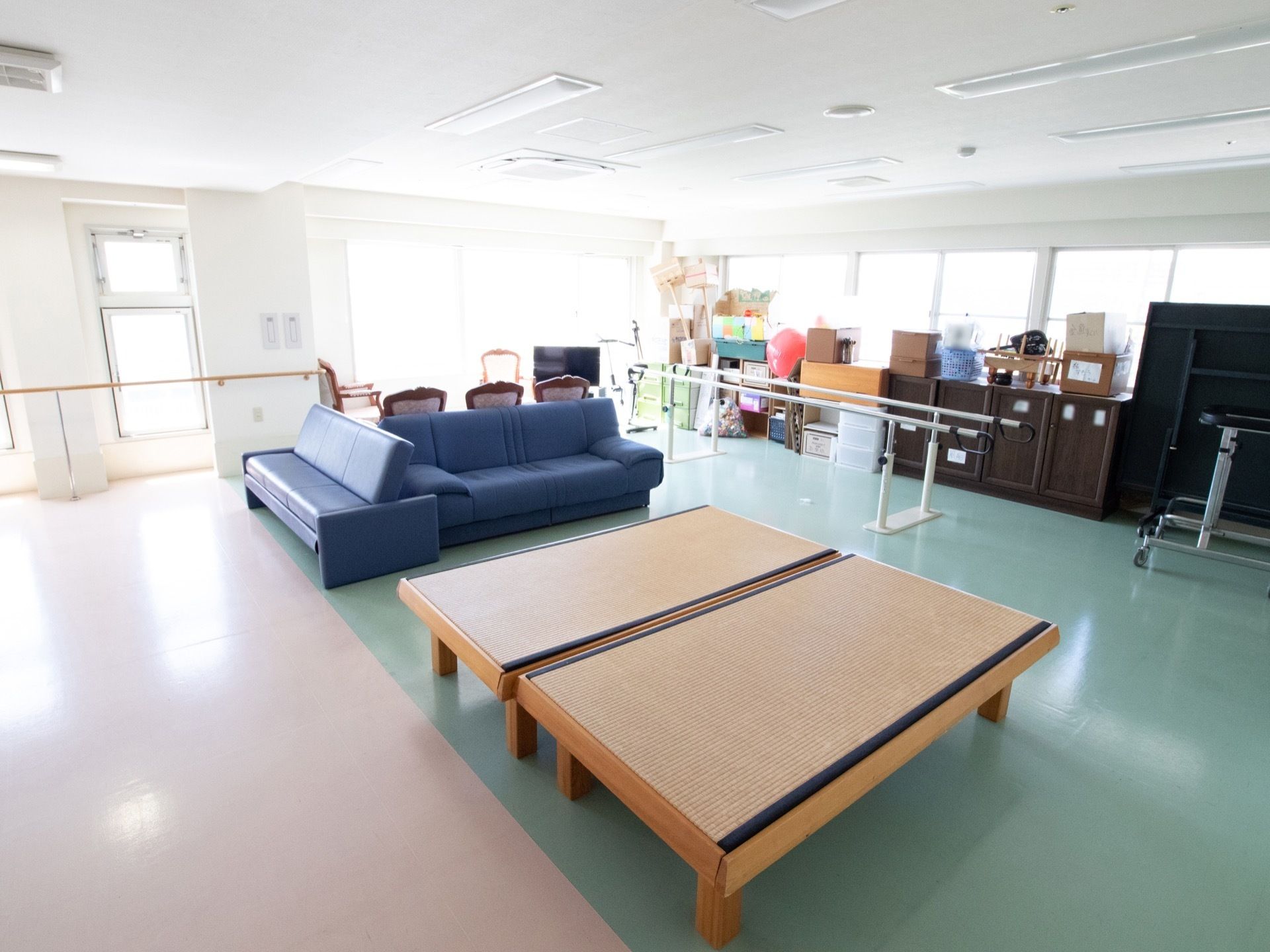 畳の敷いてある台が二つ、また、青色のソファが並べてある。部屋の奥には、歩行のリハビリに使う機器がある。