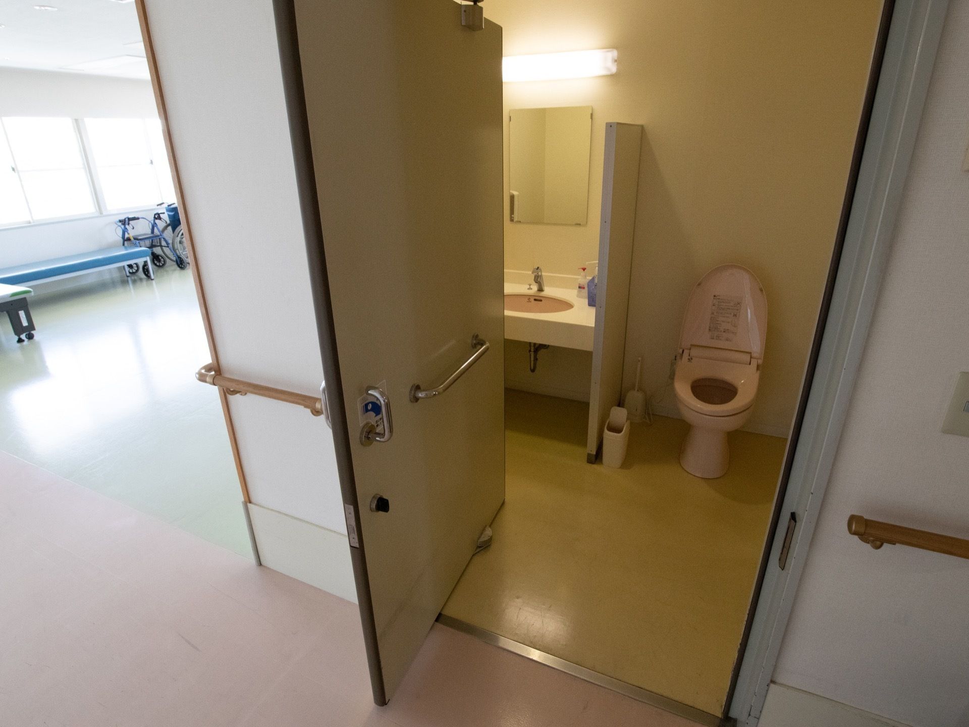 廊下にある共用のトイレである。室内には、洗面台と鏡もある。また、ドアはスライド式になっており、手すりがついている。