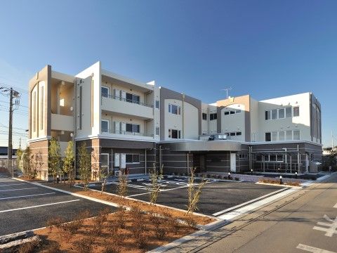 ユニークでお洒落な３階建て建物の外観である。建物前には身体障害者用の横には一般用と広めの駐車場が備わっている。