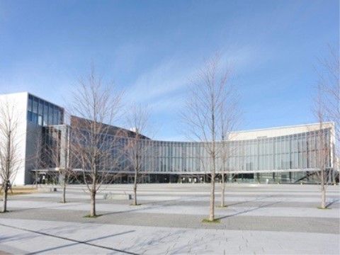 ガラス張りのカーブになった建物になっており、建物の前はとても広いスペースがある。道路側には木が間隔をあけて植えてある。