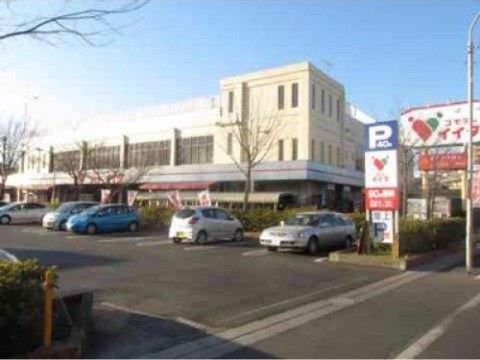 手前に駐車場が設けられ、出入口付近には駐車場の看板が設置されている。後方にはスーパーマーケットがあり、店舗前にはのぼりが立てられている。