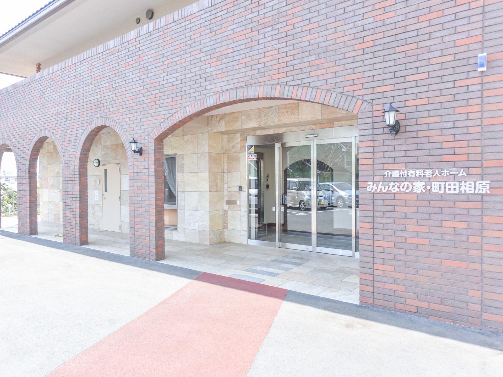 施設の玄関前の壁には施設名が白で判りやすく記載されている。玄関前はアーチ状のデザインの屋根になっていて玄関はガラス張りの自動ドア。