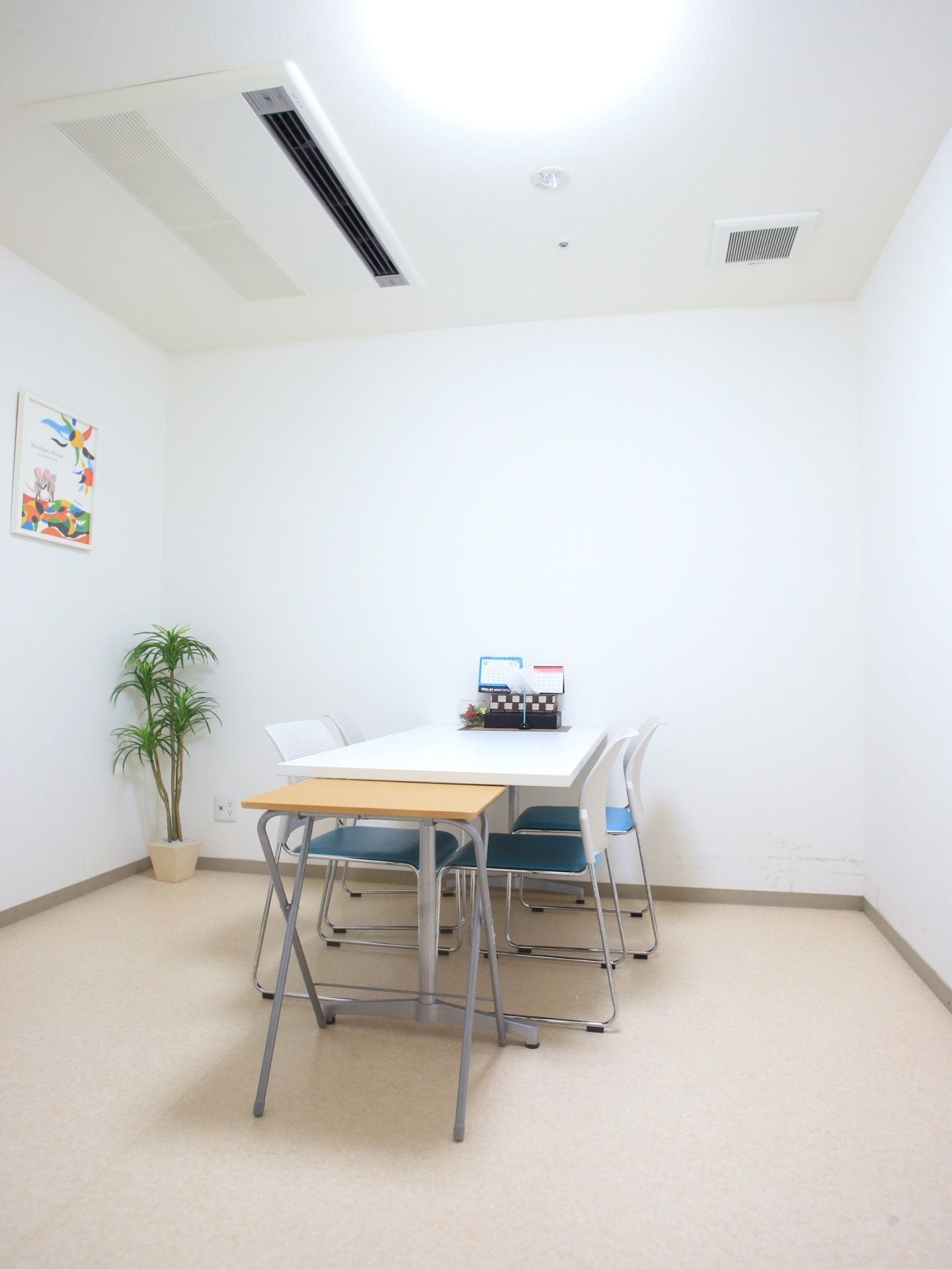 椅子が4脚とテーブルが置かれている。観葉植物が飾られている。壁には絵が掛けられている。テーブルの上にカレンダーがある。