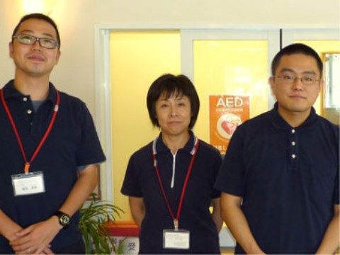 AEDの表示の前に立つ、同じ紺色の制服を着た男性2名、女性1名のスタッフ