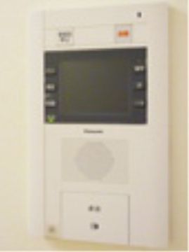 シンプルなデザインのインターフォンが設置されている。受話器を取らずにボタンを押すタイプのものである。