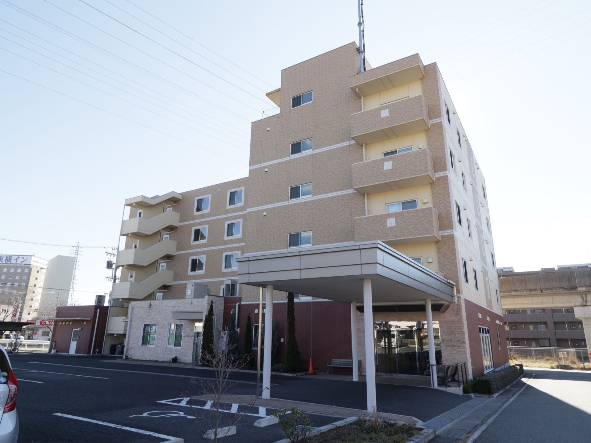 最大６階建てのベージュの建物である。玄関ポーチは屋根がせり出しており、建物の周囲には植栽が植えられている。