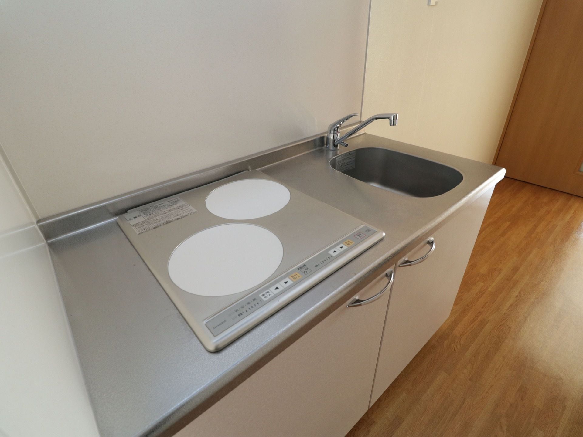 居室内に小型のキッチンが用意されている。IHタイプのコンロが２口あり、その横に流し台がある。シンク下に収納がある。