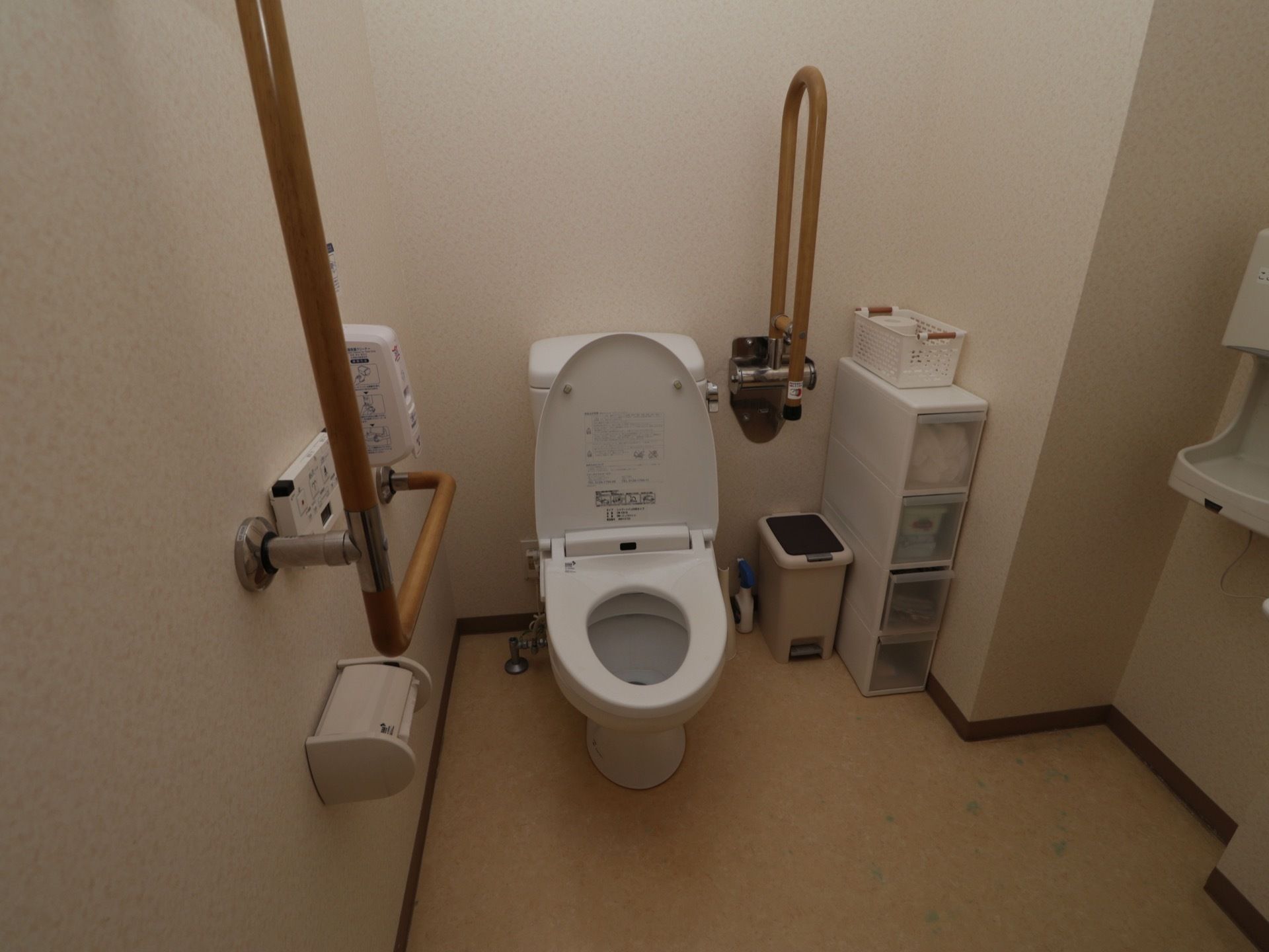 トイレの便座が開いている。壁には温水洗浄便座の操作パネルや、つかまり立ち用の手すりがとりつけられている。