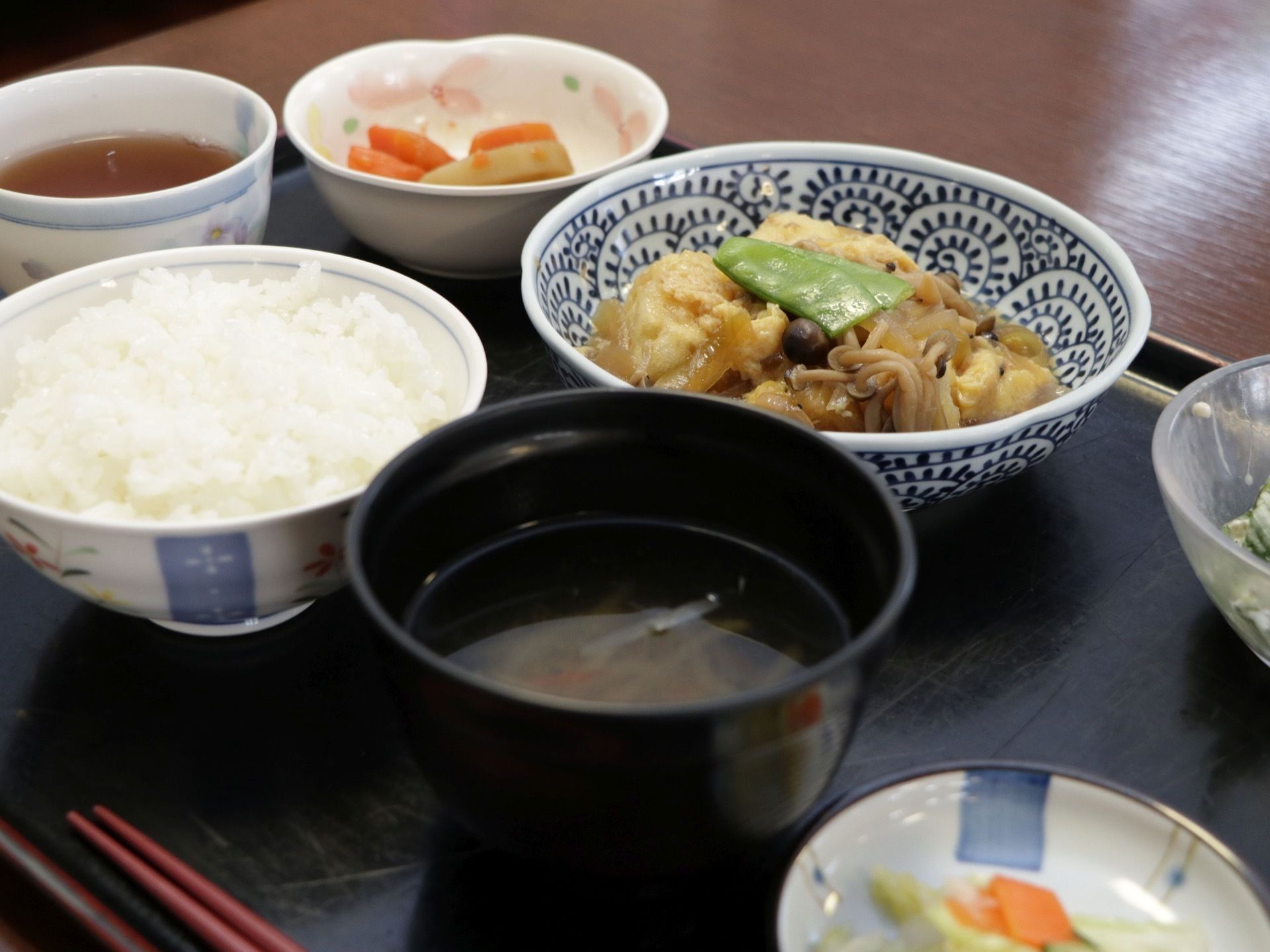木製のトレイに赤い箸が置かれている。白いごはんとわかめの味噌汁、メインは肉じゃがである。おひたしやおしんこもついている。