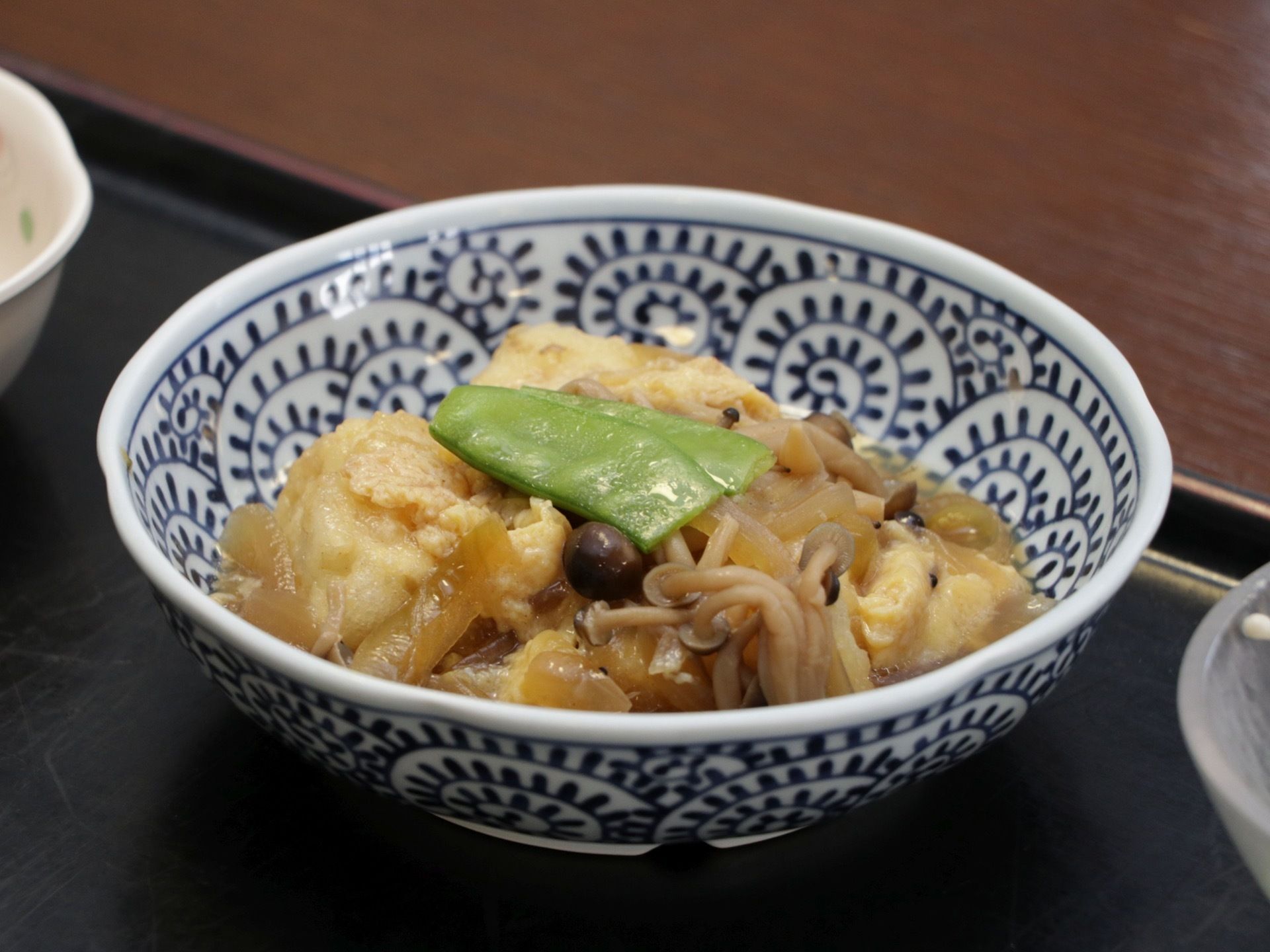 野菜とお豆腐の煮物が器に盛りつけされている。他のおかずの入った器と一緒に黒いプレートに並べられている。