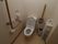白を基調とした清潔感のある明るいトイレである。立ち上がりや座る際のサポートになるバーが完備されている。