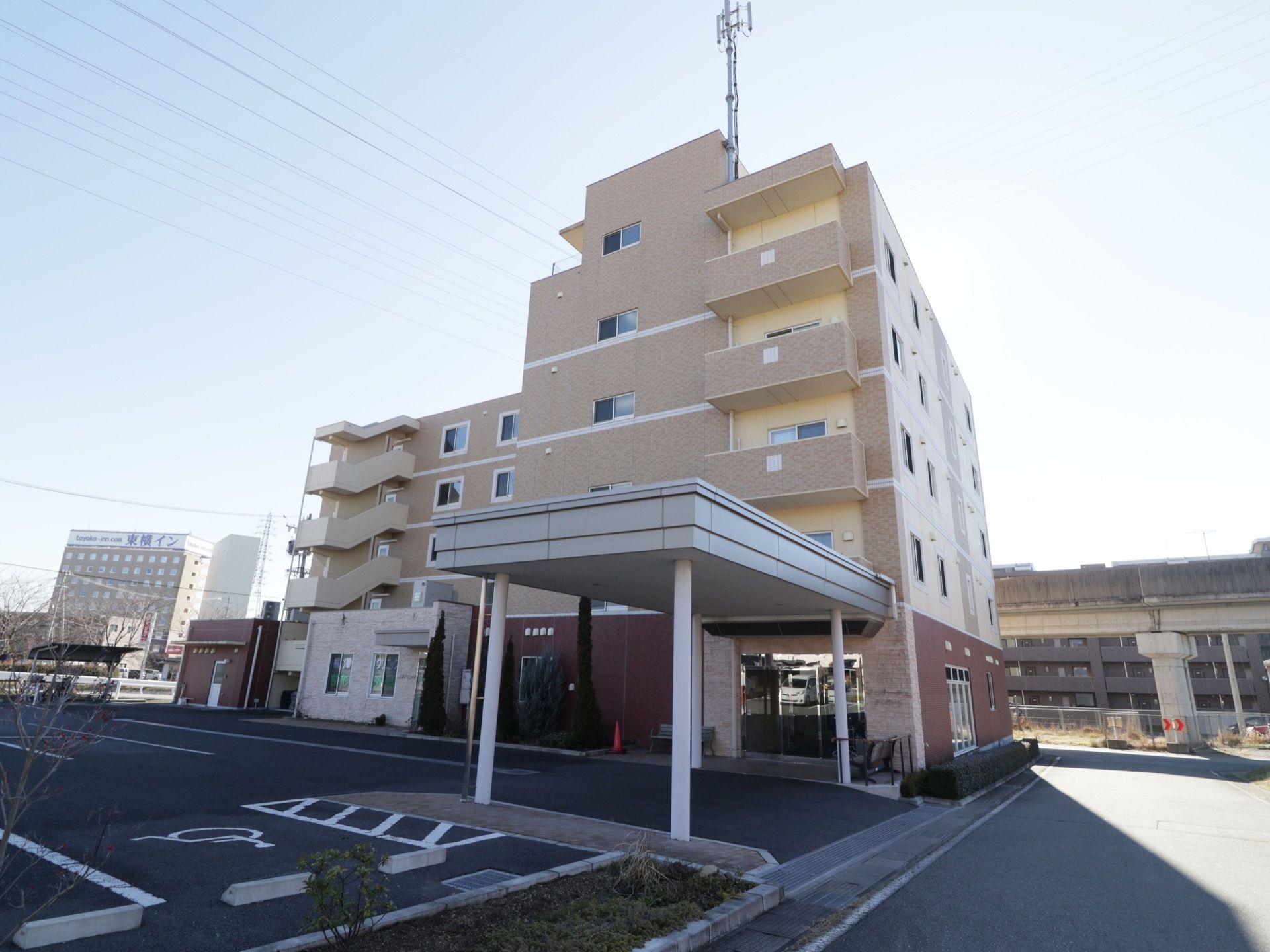 高級マンションを思わせるような５階建てのブラウン系の建物である。建物の周りには駐車スペースがたくさん用意されている。