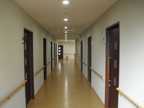 廊下の壁にはしっかりとした手すりが取り付けられている。手すりと手すりの合間に、モダンな印象の木製の居室の扉が並んでいる。