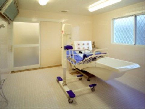 床と壁が白い浴室は開口部が広く、扉にはすりガラスが入っている。特殊介助浴槽と、電動リフトが置かれている。