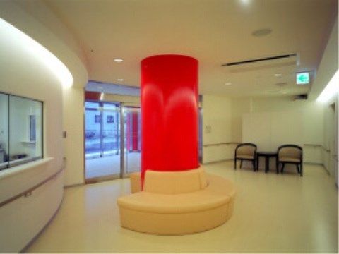 中央には赤い柱があり、白いソファが円形に、取り巻くように置いてある。手前にはガラス窓付のカウンターがあり、壁には手すりが付いている。
