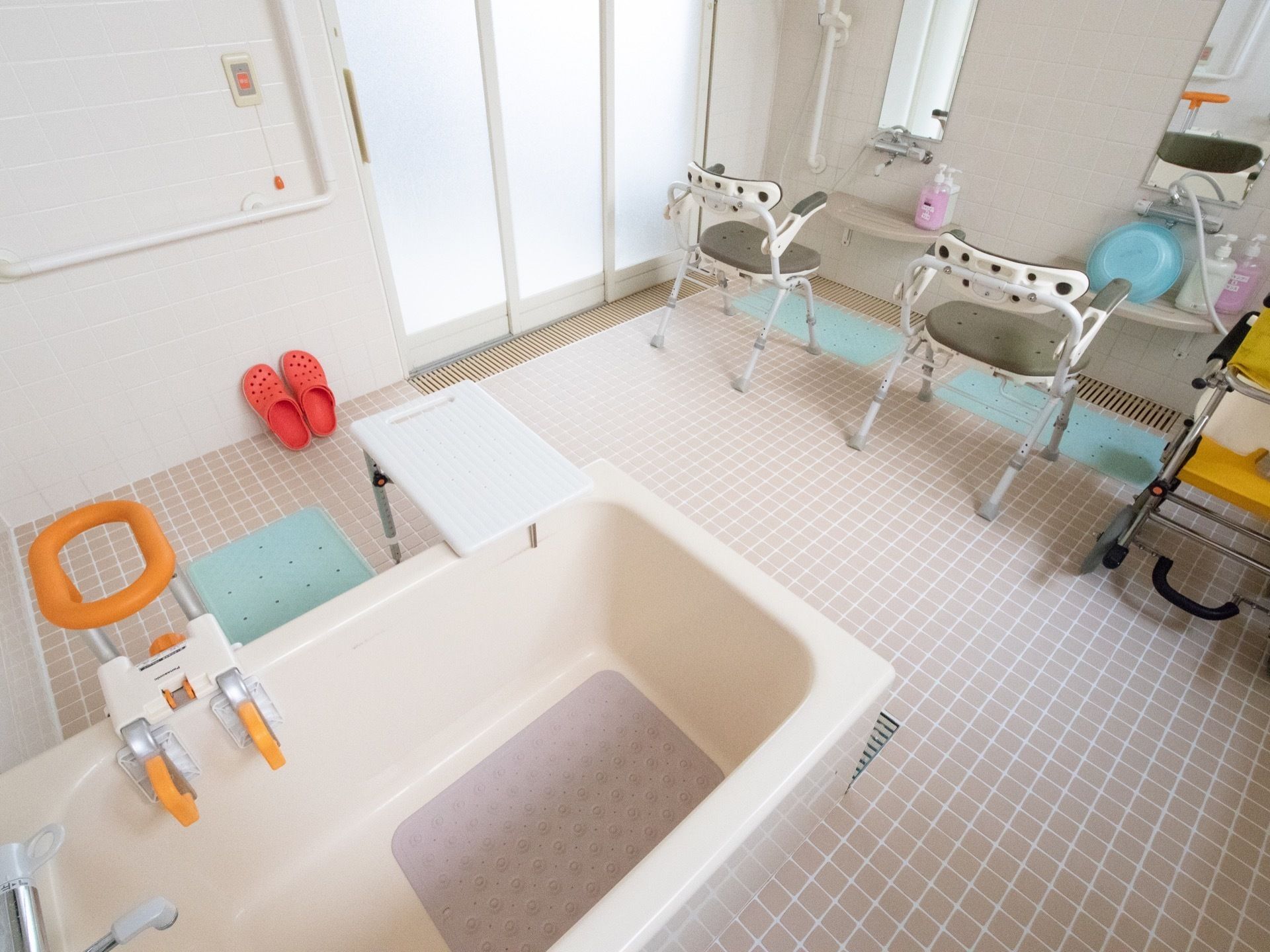 浴室には介護用の椅子が２脚用意されており、洗面器やシャンプー類が置かれている。浴槽には移動補助用の手すりが設置されている。