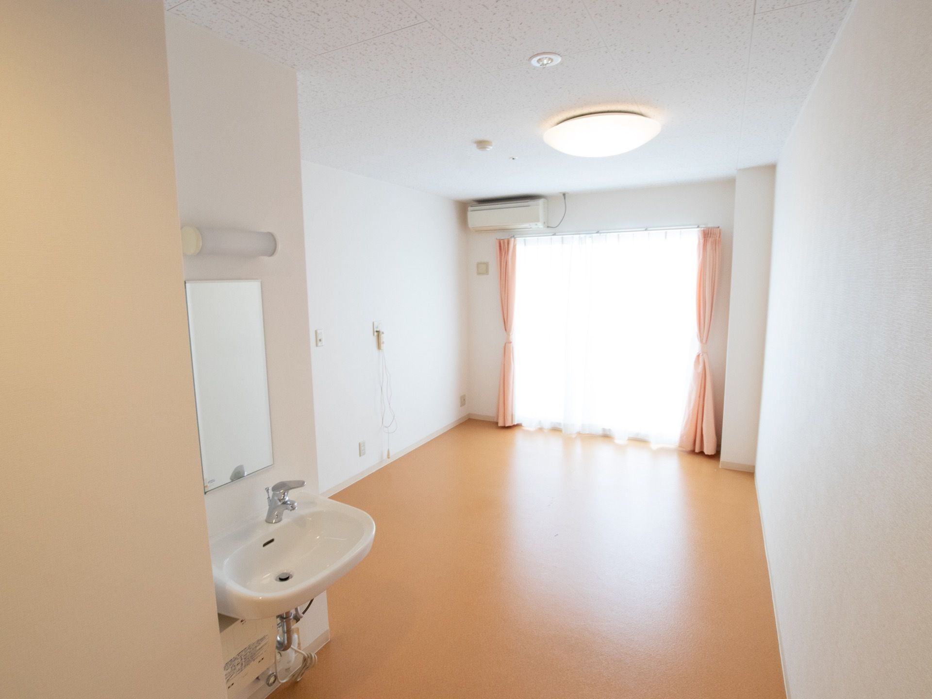 部屋の天井の中心には橙色の電気が備え付けられている。また、水道や空調設備もあり、奥の壁に大きな窓がある。