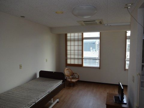 室内にはベッド、テレビ、椅子が配置されている。窓には転落防止ガードが取りつけられている。天井には空調が設置されいている。