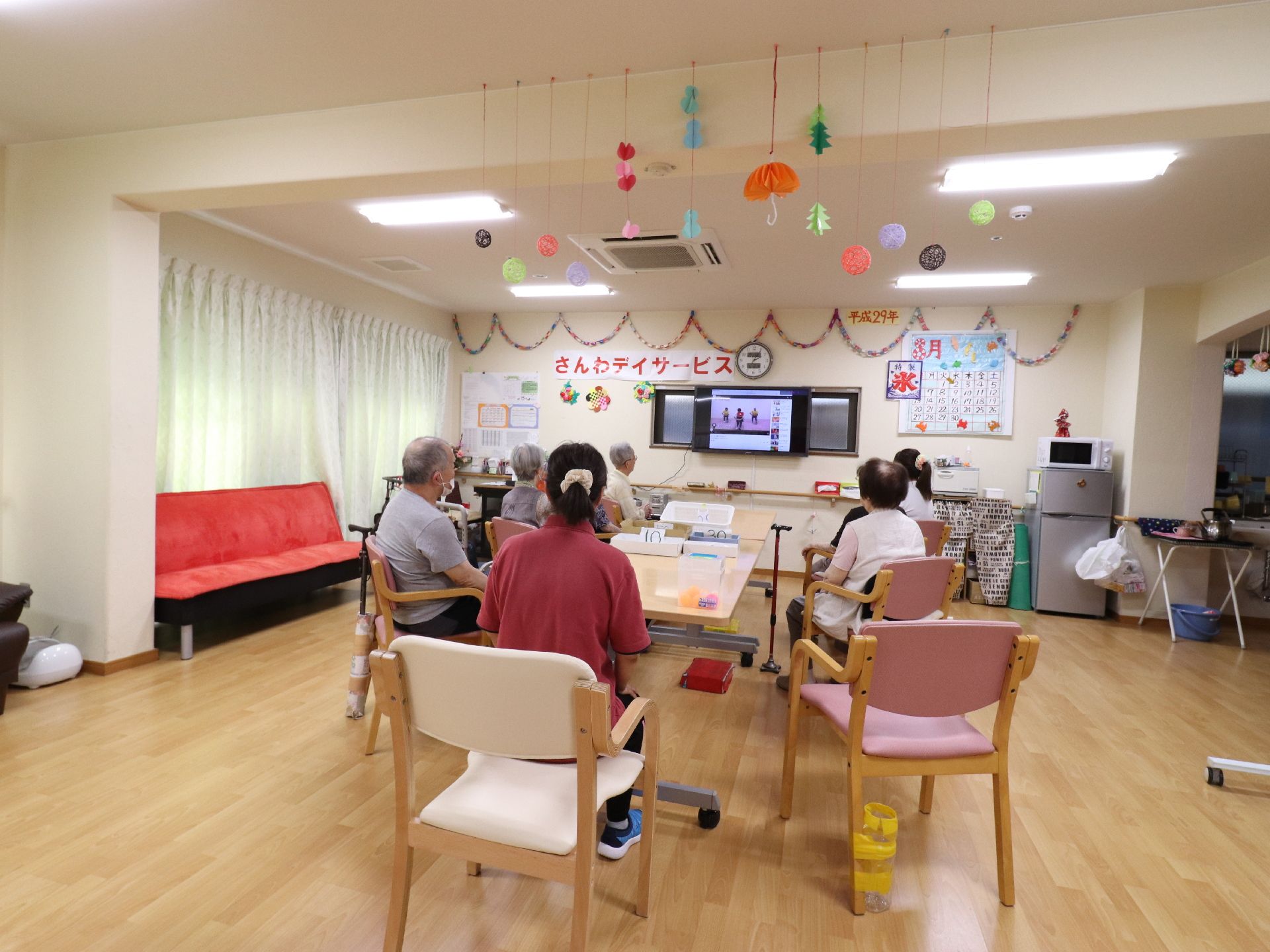 窓にはカーテンがかかっていて、閉じてある。壁には、手書きでいろんなものが貼ってある。テレビを見ている。