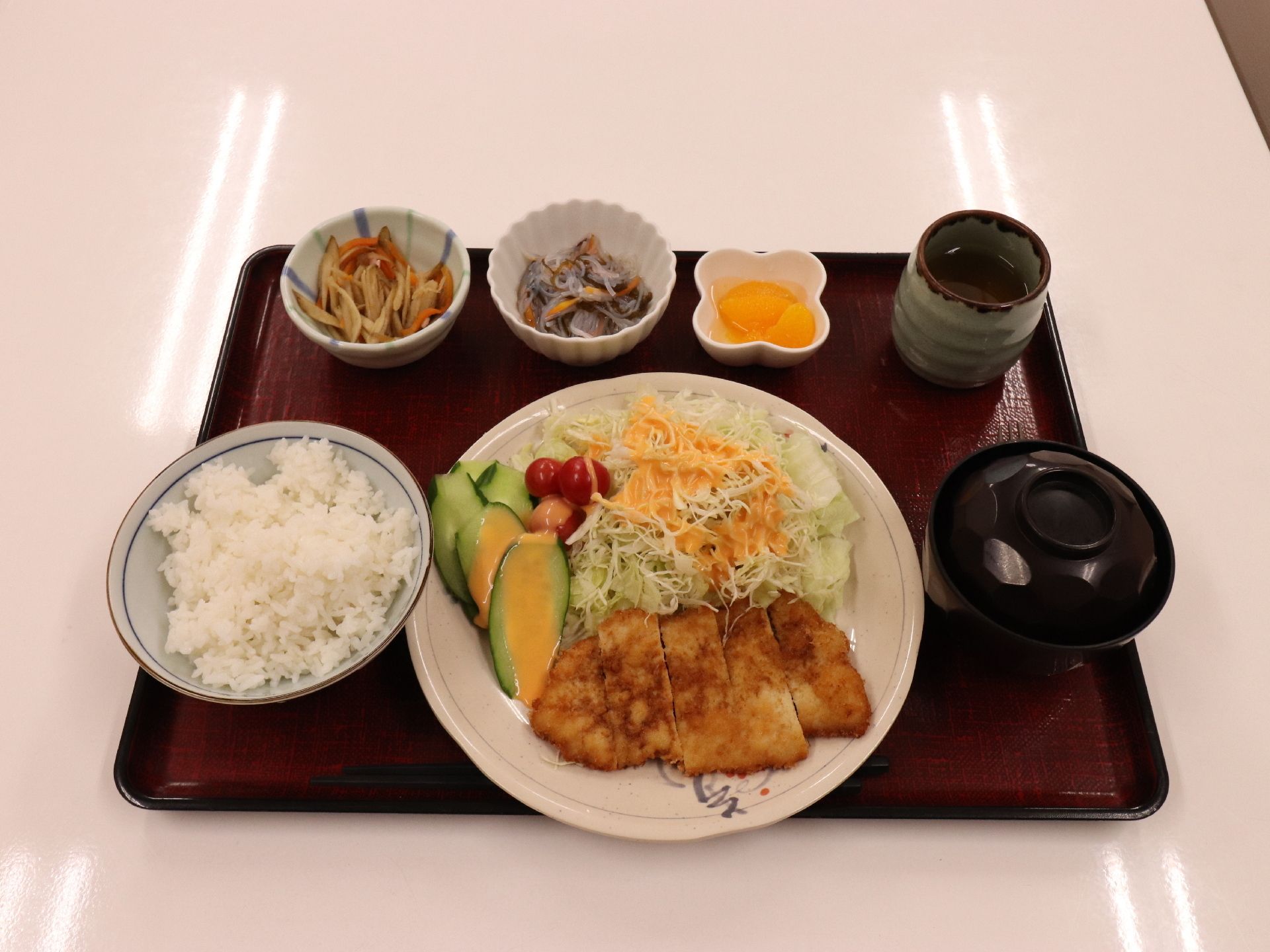 盆の上にごはん、味噌汁が乗っている。おかずはプレートに野菜と一緒に盛り付けてあり、食べやすい大きさにカットしてある。
