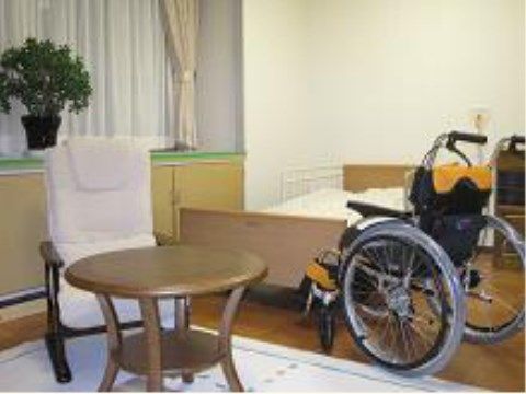 ホテルの1室のような落ち着いた雰囲気の居室。小さめの丸いテーブルのそばに、座り心地の良さそうな白い椅子が置いてある。