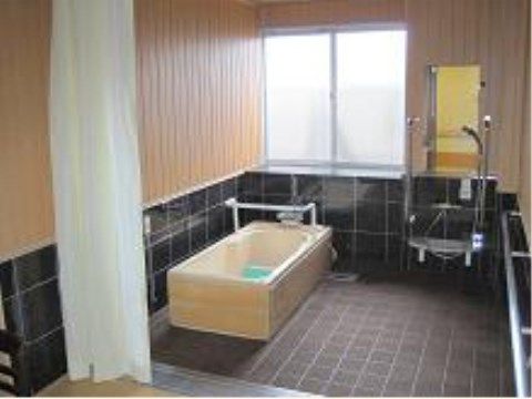 黒いタイルに木目調の壁がモダンなデザインの浴室である。壁には洗い場まで続く手すりがついていて、安全に移動できる。