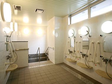シャワーと鏡の横に手すりをつけた共同の広々とした風呂場