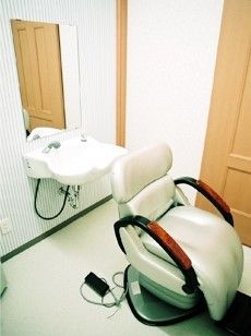 シャワー式の洗面台の前に、白色の理容用椅子が設置されている理容室