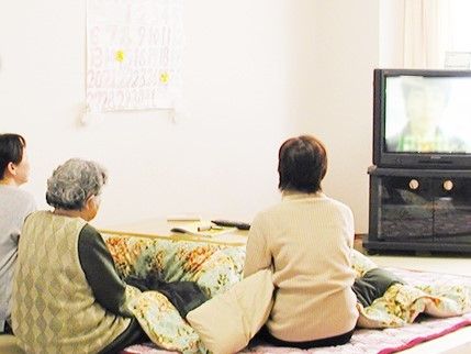 コタツに入ってテレビを観ながら談笑する3人の女性たち