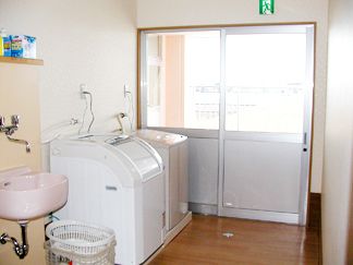 白い洗濯機が2台並んでいる部屋に、洗剤や洗濯カゴも置かれているランドリールーム